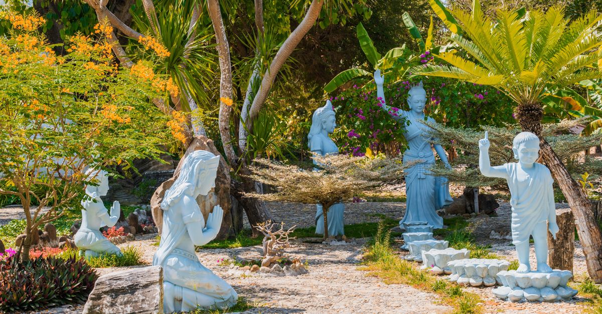 Peaceful outdoor garden with blue statues amid tropical foliage under a sunny sky.